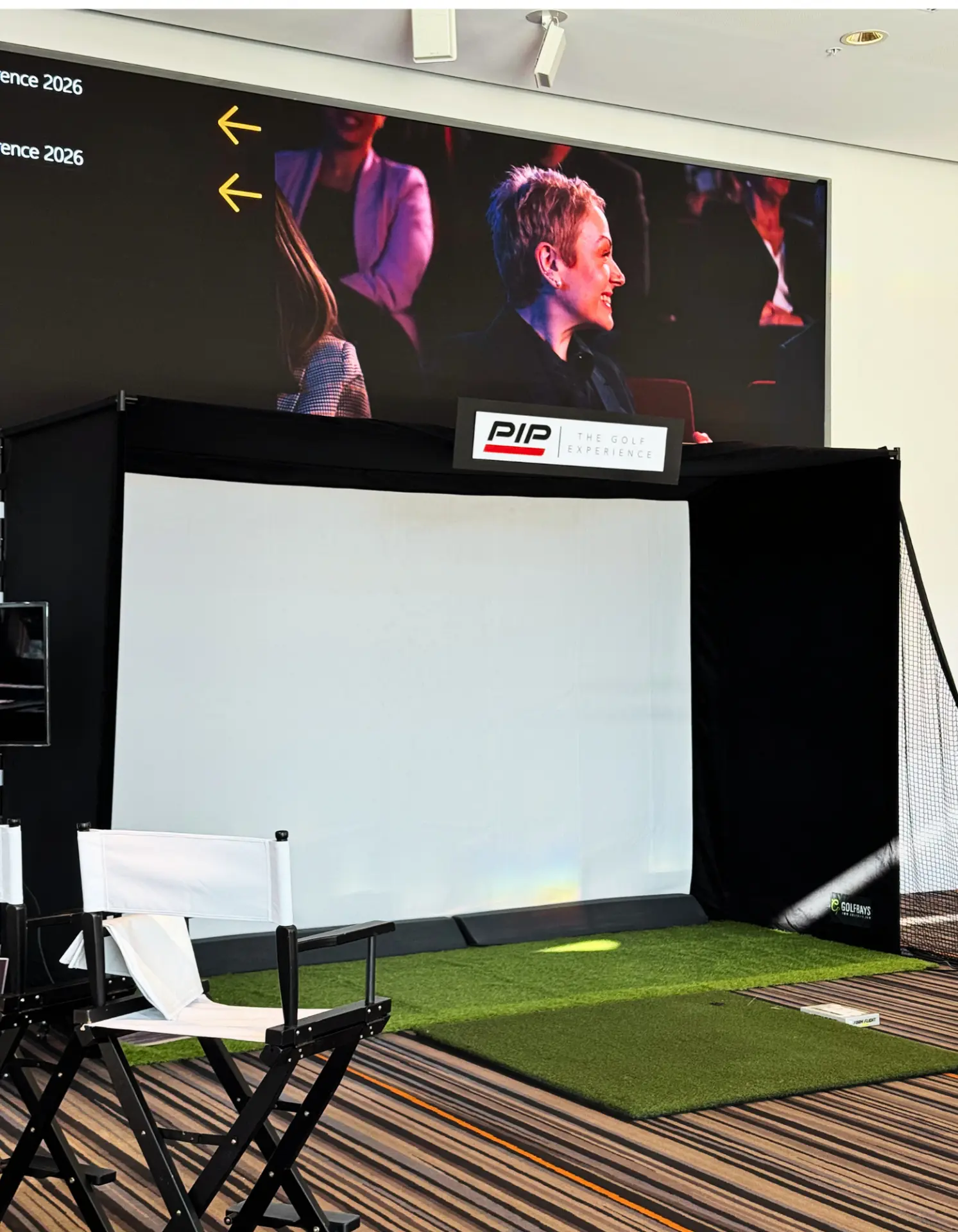 Full Send golf simulator booth at a corporate conference with directors' chairs and PIP The Golf Experience branding