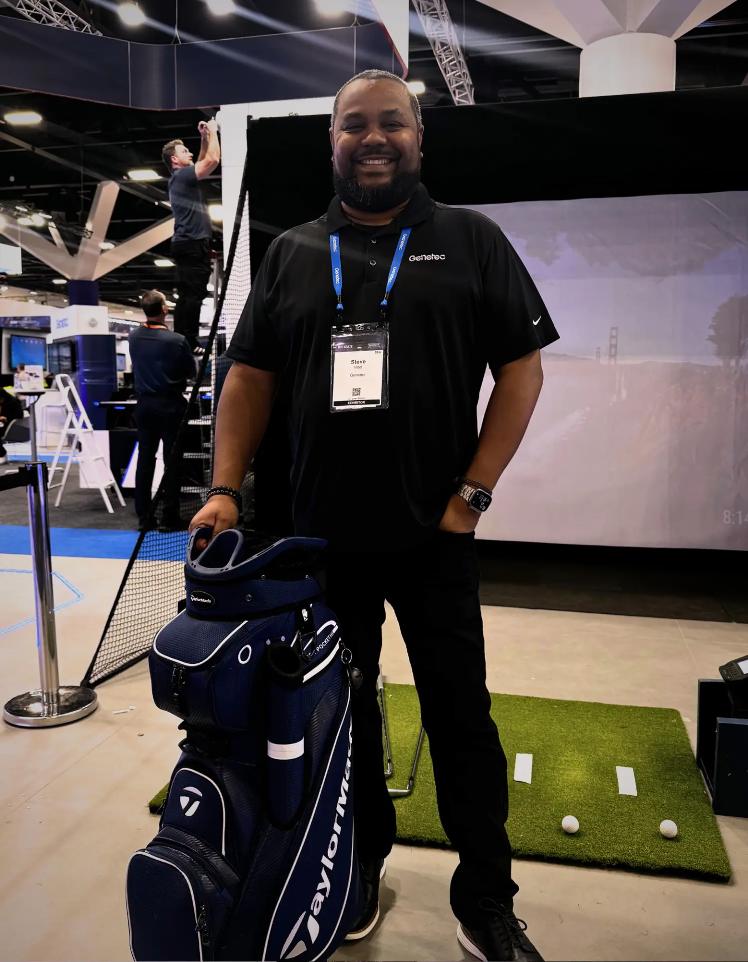 Trade show guest collecting a TaylorMade tour bag prize beside the Full Send golf simulator at the Integrate expo in Adelaide