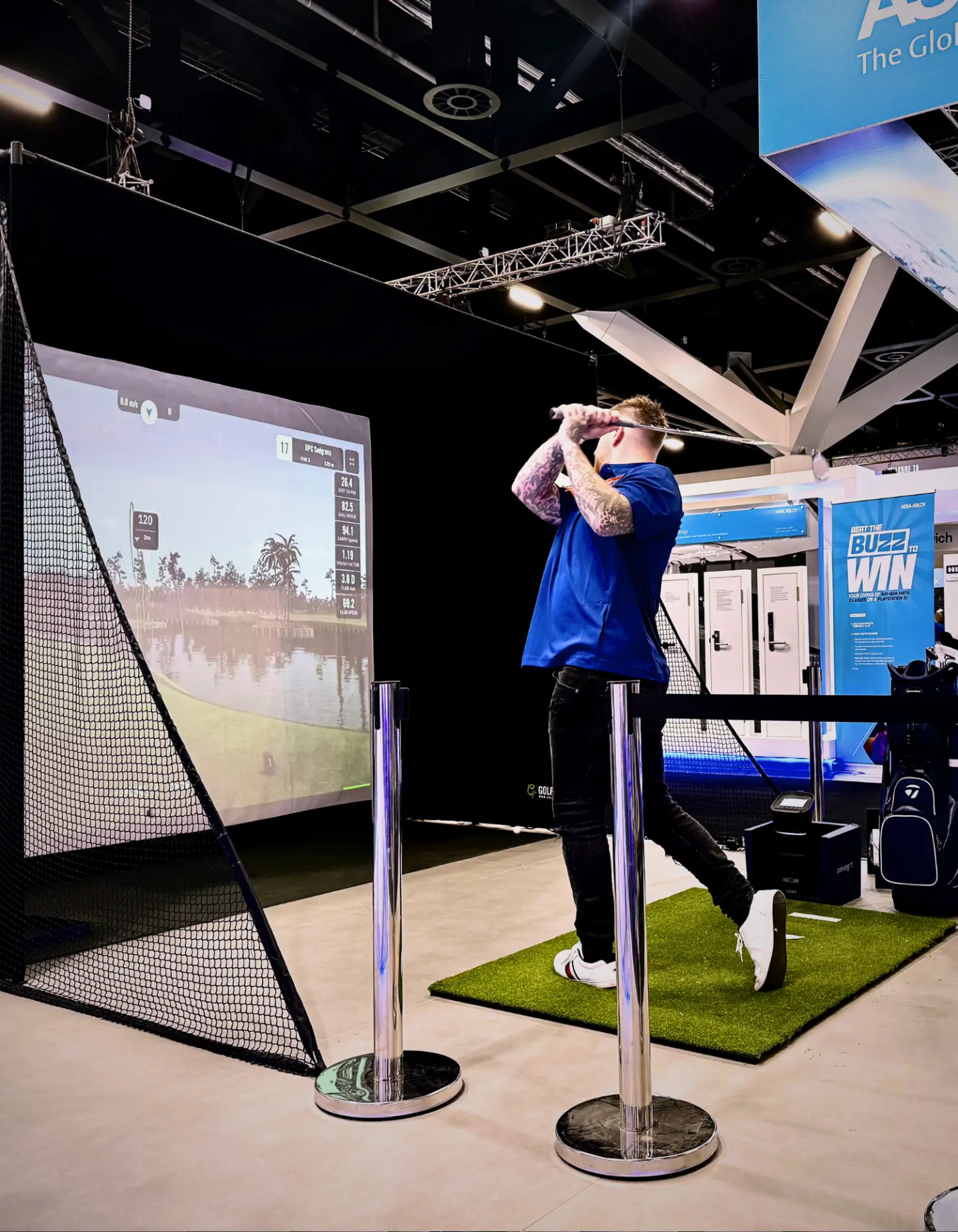 Guest mid-swing on an exhibition golf simulator activation behind crowd barriers at an Adelaide trade show