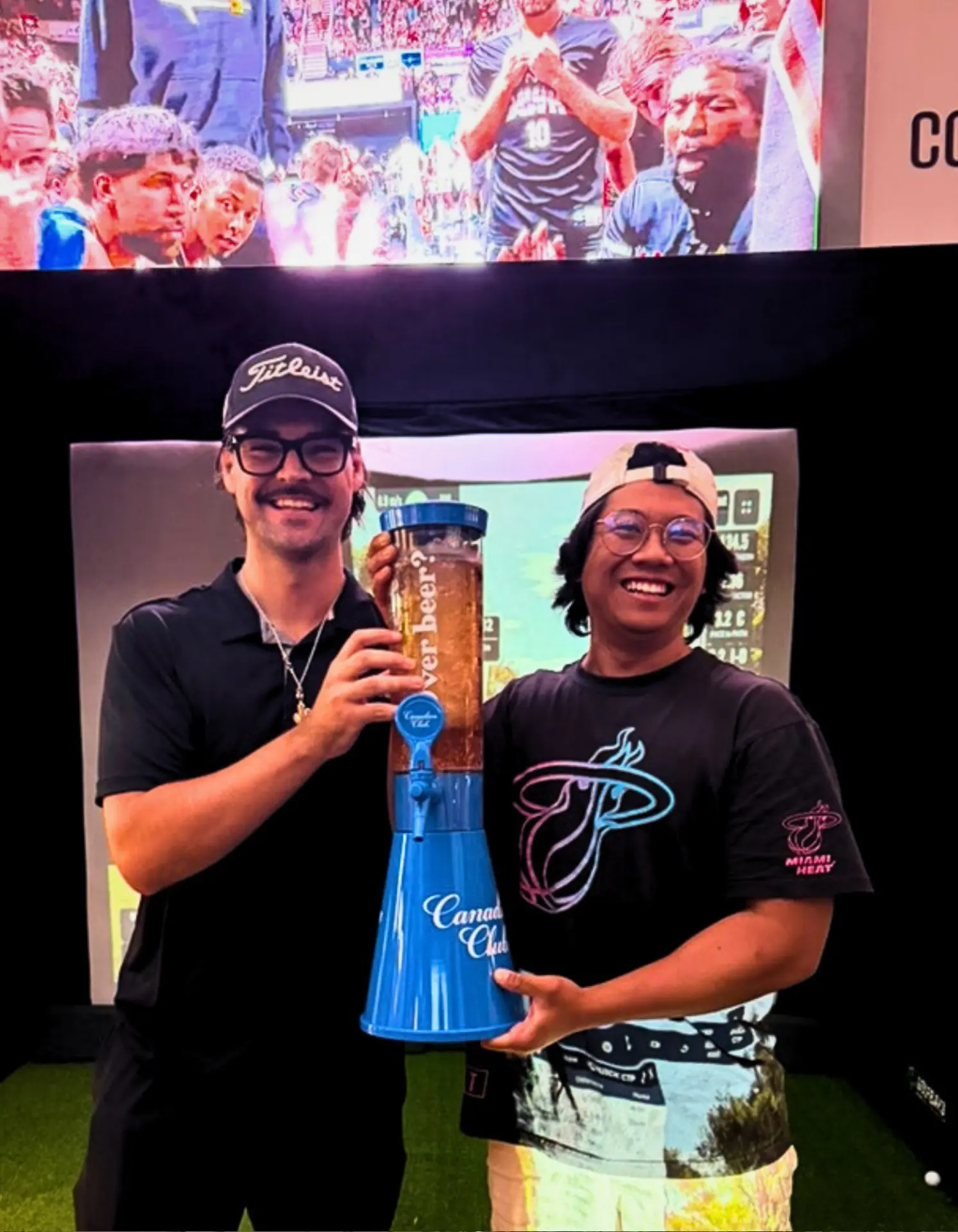 Tournament winners celebrating with a beer tower prize in front of the Full Send golf simulator
